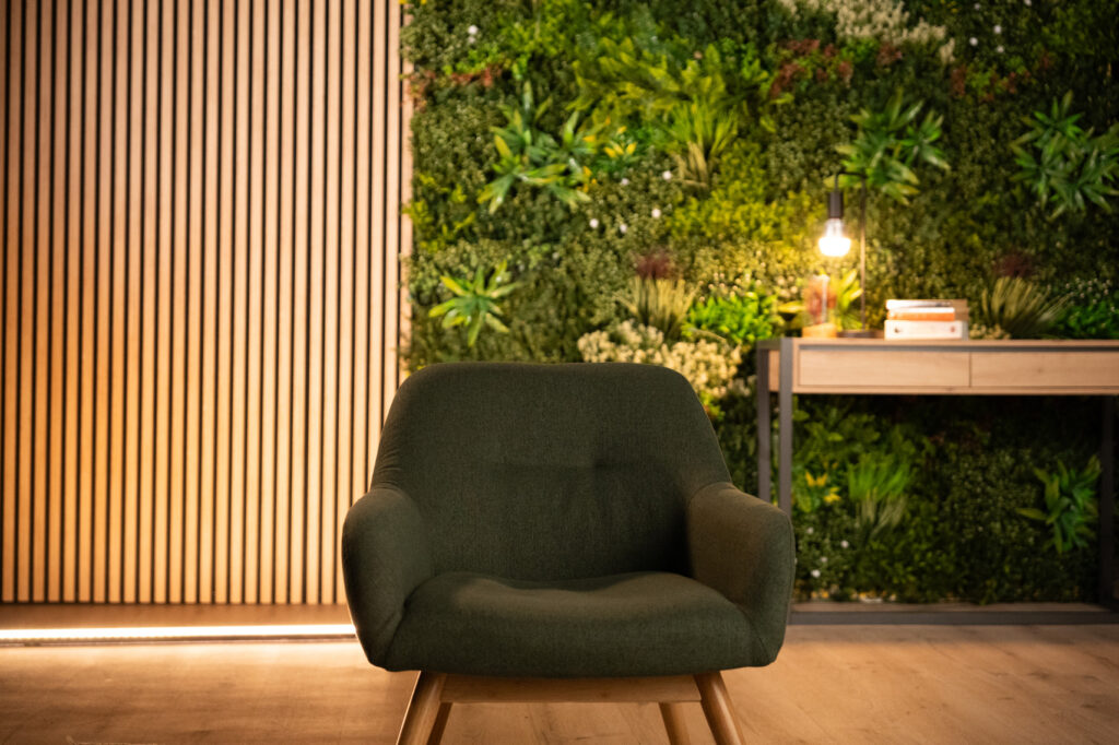 Fauteuil vert en plan rapproché, devant le mur végétal et le panneau en tasseaux bois.
