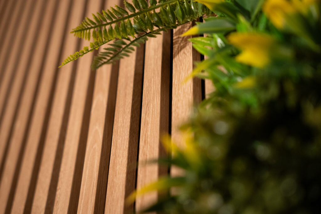 Gros plan sur le panneau en tasseaux bois qui accompagne le mur végétal du décor L’Équilibre.