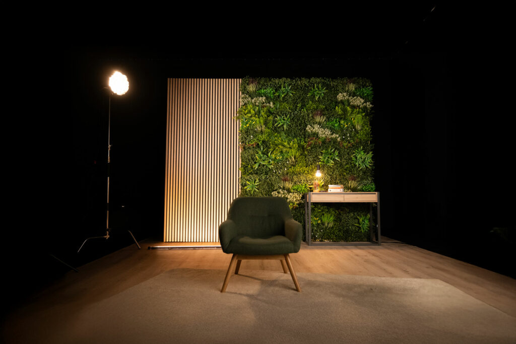 Vue d’ensemble du décor L’Équilibre avec mur végétal, fauteuil vert et bureau bois clair, prêt à tourner.