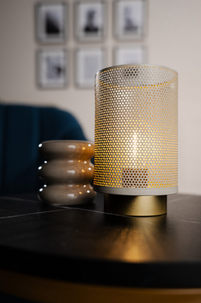 Gros plan sur une bougie allumée dans une lampe en métal perforé, posée sur une table noire du décor La Parenthèse.