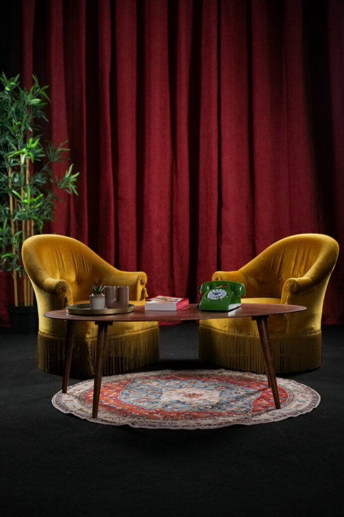 Vue centrée sur deux fauteuils jaunes face à face, avec une table basse et un rideau rouge en fond