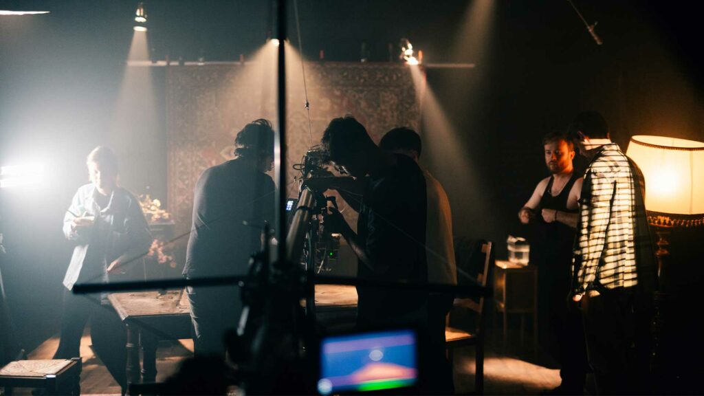 tournage-clip-bts Équipe technique filmant une scène de clip dans une ambiance tamisée et dramatique.