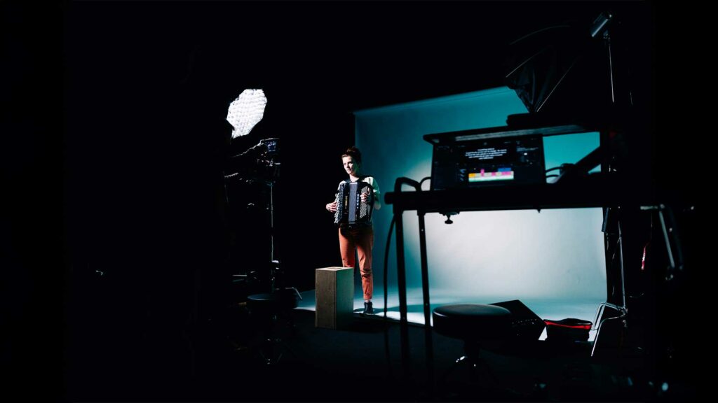 tournage-clip-musique-bts2 Musicienne jouant de l’accordéon sur fond bleu dans un studio de tournage.