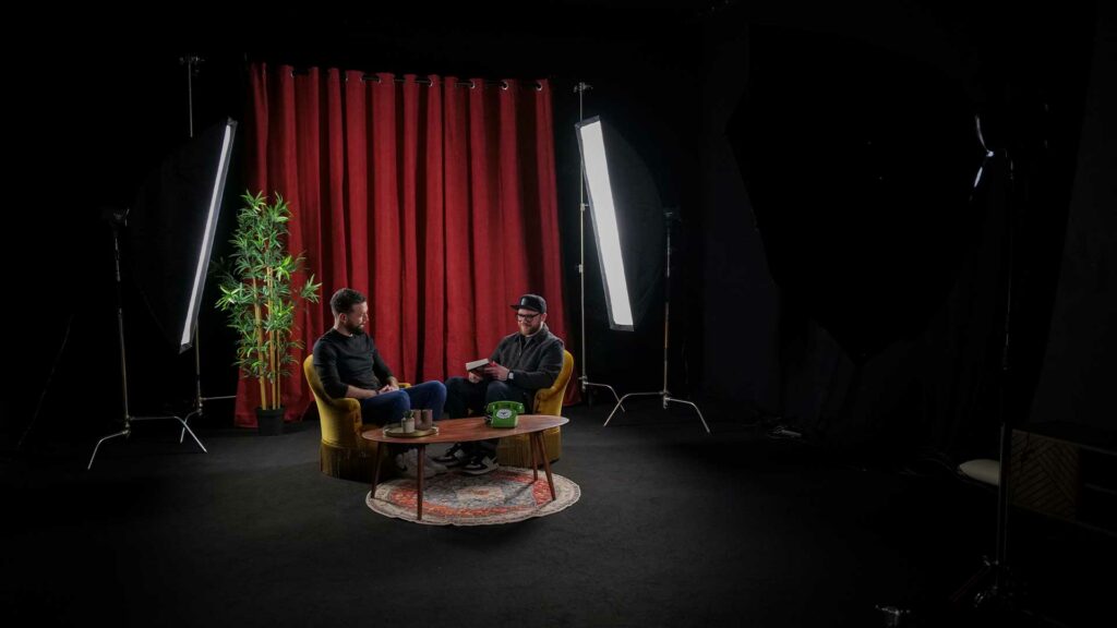 tournage-emission-bts Deux personnes en tournage d’émission, éclairées dans un studio avec fond rouge.