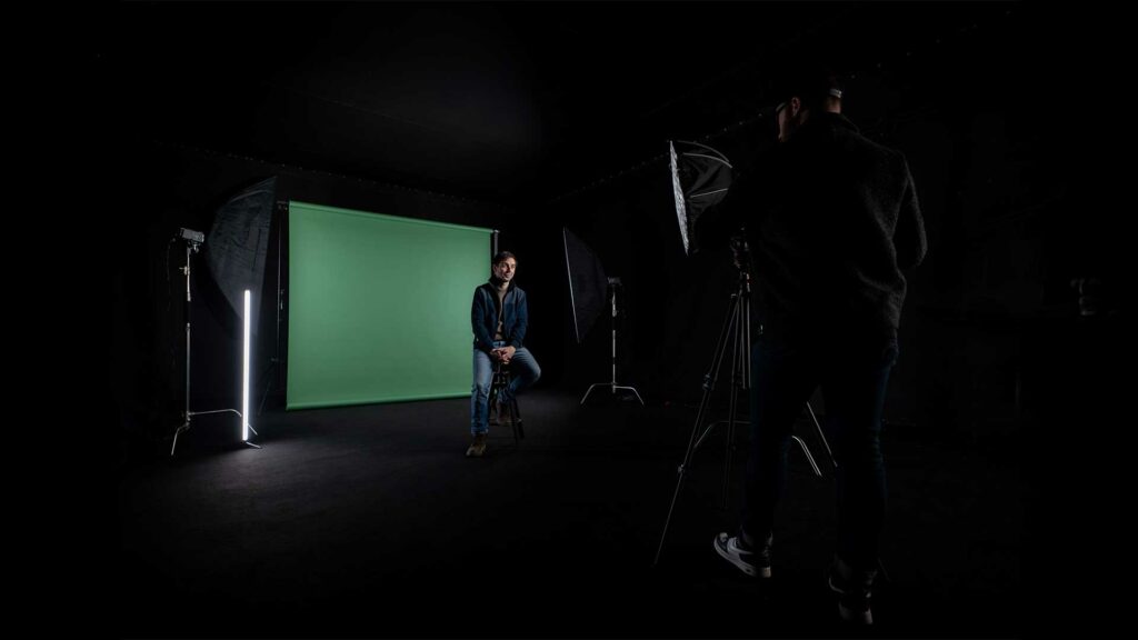 tournage-fond-vert-bts Tournage face caméra avec un fond vert et installation lumière dans un studio noir.
