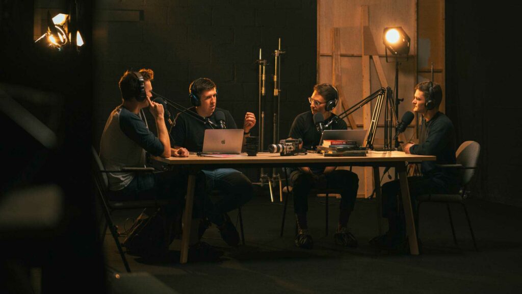 tournage-podcast-table-bts Enregistrement d’un podcast à quatre micros autour d’une table dans un studio sombre.