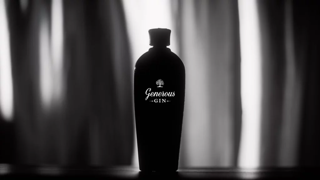 generous-gin-silhouette-packshot-noir-et-blanc-studio-401 Photographie publicitaire en noir et blanc pour la marque "Generous Gin", réalisée au Studio 401 à Rennes. La bouteille est présentée en silhouette grâce à un contre-jour maîtrisé, mettant en valeur ses courbes élégantes et le logo blanc qui se détache du verre sombre. Le fond est constitué d'un voilage flou avec des jeux de lumière verticaux. Ce visuel artistique démontre l'expertise du studio pour des packshots de luxe au rendu minimaliste et cinématique.
