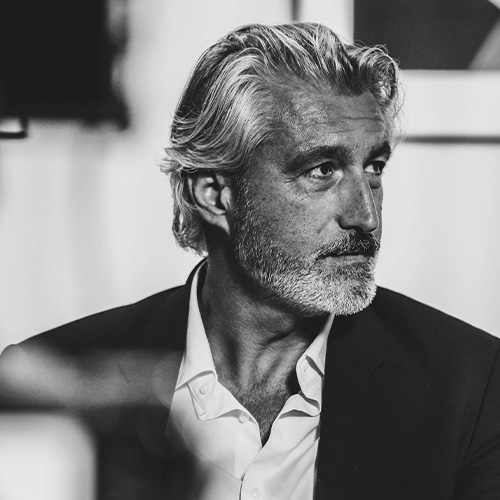 studio-video-rennes-portrait-noir-et-blanc-tournage-interview Portrait en noir et blanc d'un homme d'âge mûr aux cheveux poivre et sel et barbe soignée, portant un costume et une chemise blanche. La photo, prise avec un éclairage contrasté au Studio 401 à Rennes, illustre le rendu professionnel et cinématographique d'un intervenant lors d'un tournage d'interview ou d'un film institutionnel réalisé sur le plateau.